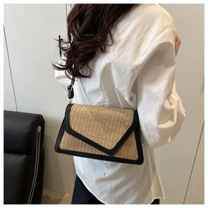 Detail of straw envelope bag with black leather trim worn on white shirt