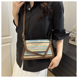 Detail of colorful woven straw envelope bag with brown leather trim worn by model