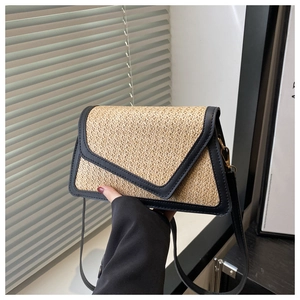 Detail of woven straw shoulder bag featuring black leather flap and gold metal hardware
