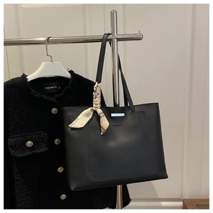 Détail du sac cabas en cuir noir avec barre en métal, foulard en soie et texte imprimé