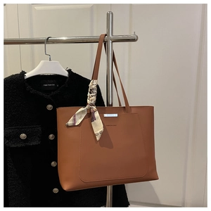 Détail d'un sac cabas en cuir marron avec barre métallique et foulard en soie sur la poignée