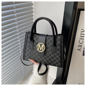 Detail of black tote bag with M-pattern print and golden metal M-logo buckle