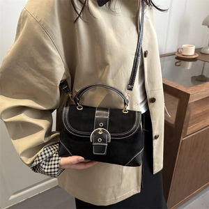 Vintage black crossbody bag with gold buckle and white stitching on khaki trench coat