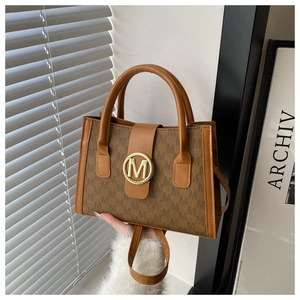 Close-up of monogrammed crossbody bag with golden M metal buckle and twin handles