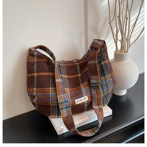 Detail of vintage plaid tote bag with wool texture and adjustable strap on a white book