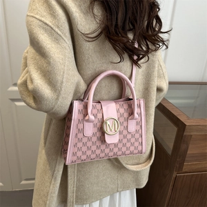 Pink monogram trapezoid handbag with gold M logo and shoulder strap on beige coat