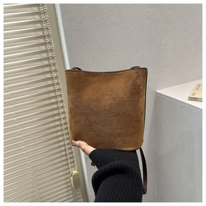 Détail du sac seau en daim marron foncé avec fine bandoulière porté à la main