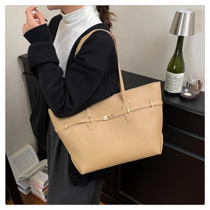 Dettaglio di una borsa tote in pelle beige con fibbia dorata indossata da una modella
