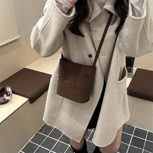 Sac seau minimaliste en daim marron foncé avec fine bandoulière porté par un mannequin