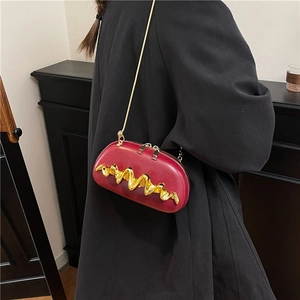 Deep red oval crossbody bag with wavy gold metal trim and chain strap shown on model