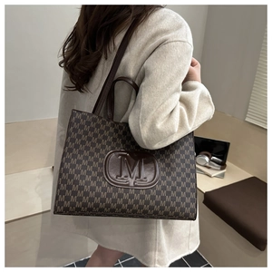 Detail view of the brown monogram tote bag featuring a prominent embossed M logo patch
