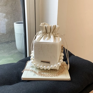 Détail du sac seau blanc avec poignée en perles, chaîne dorée et texture verticale