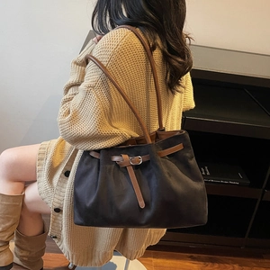 Minimalist black tote bag with brown leather straps and buckle, shown on a model