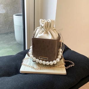 Détail d'un mini sac marron avec poignée en perles et chaîne dorée sur un livre blanc