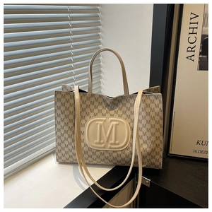 Detail of cream tote bag with monogram print and embossed logo on leather patch