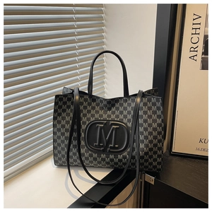 Macro shot of M-letter print texture and black logo plaque on large tote bag