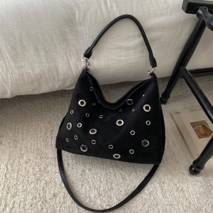 Detail of black suede motorcycle bag with silver metal eyelets on a soft rug