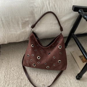 Detailed macro view of a brown suede shoulder bag featuring silver metal eyelet decorations