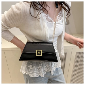 Detail of black matte leather crossbody bag with golden M metal buckle on a white sweater
