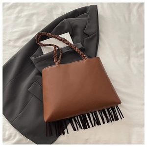 Detail of a brown leather bucket bag with woven handles and long decorative tassels