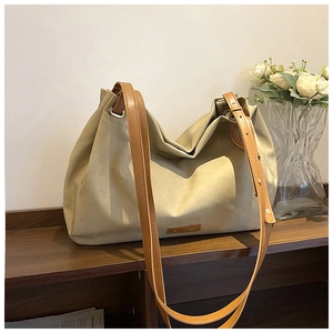 Detail view of large beige tote bag with adjustable brown strap on wooden surface