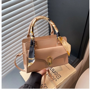 Detail of beige PU leather handbag featuring a gold twist lock and silk scarf handle wrap