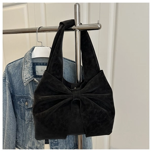 Detail of black suede shoulder bag featuring a large bow and soft vintage texture