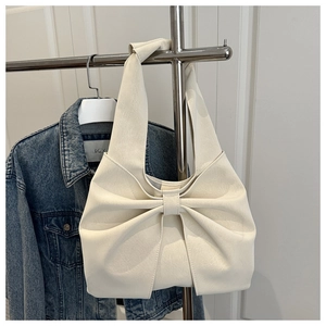 Detail of creamy white underarm bag featuring a large decorative bow and soft PU leather texture