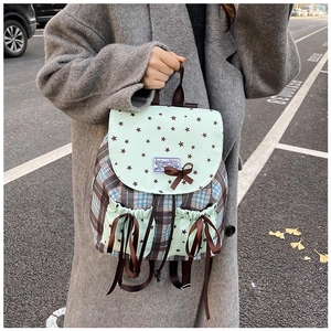 Detail view of mint green backpack with star prints, brown bows, and plaid side textures
