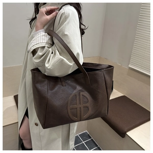 Detailed shot of brown matte lychee leather texture and circular logo on large tote bag