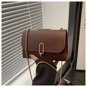 Detail of a brown leather shoulder bag featuring a gold chain and oval metal buckle closure