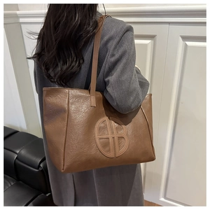 Macro detail of brown leather tote bag showing a round embossed logo and textured finish