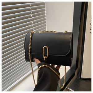 Detail of black crossbody bag featuring a golden oval metal clasp and fine chain strap