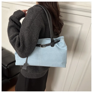Detail of light blue denim tote bag featuring black leather straps and metal buckles