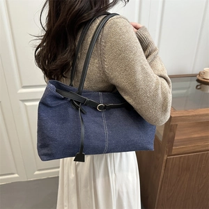 Large denim tote bag with black leather straps and metal buckles shown on a shoulder