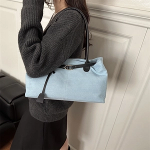 Blue denim tote bag with black leather straps and metal buckle shown on a model