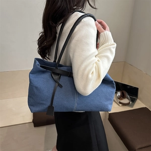 Large blue denim tote bag with black straps worn by a model in a cozy cafe setting