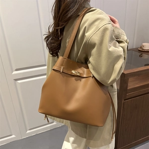Minimalist brown leather bucket bag with gold clasp and shoulder straps in urban setting