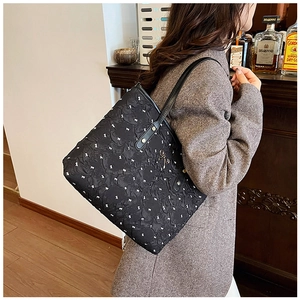 Gros plan sur le tissu du sac cabas noir à motifs nœuds blancs et pendentif doré
