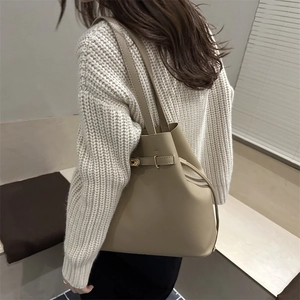 Minimalist khaki leather bucket tote bag with metal lock shown in a stylish commute setting