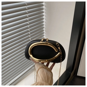 Detail of black pebbled leather bag with gold crescent handle and metal chain strap