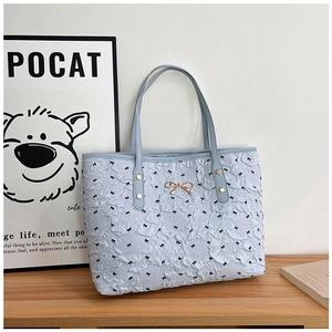 Détail du sac cabas bleu clair avec texture plissée et imprimé nœuds noirs avec accent doré