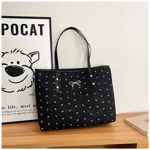 Détail d'un sac cabas noir matelassé avec des motifs de nœuds blancs et accents dorés