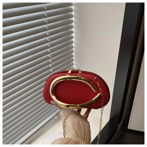 Detail of red pebbled leather semi-circle clutch with sculptural gold metal handle and chain
