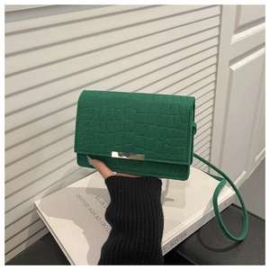 Detail of dark green crocodile embossed handbag with long gold metal buckle on white books