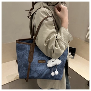 Detail of dark blue denim tote with brown leather handles and plush cloud charm