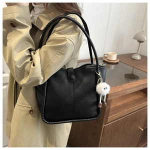 Detail of a black leather bucket bag with a cute plush monster charm on a trench coat
