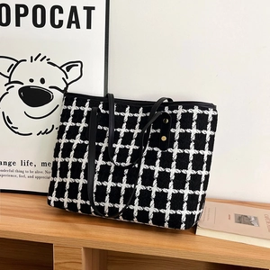 Large capacity black and white tweed tote bag with leather straps on a bookshelf