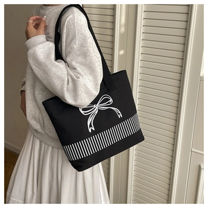 Detail of black canvas tote bag with white bow embroidery and striped pattern