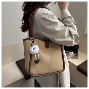 Detalle de un bolso tote beige y marrón con un lindo colgante de pelo en forma de ojo